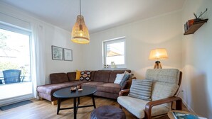 A cozy living room with a brown leather sofa, a wooden coffee table, a cushioned armchair, and a hanging pendant light. - Ferienhaus Anker - Ferienhaus Anker auf Rügen (Garz/Rügen)
