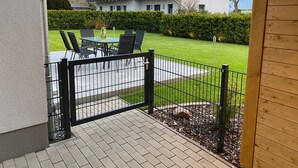 Un'area patio con tavolo e sedie, una recinzione in metallo nero e un prato curato.