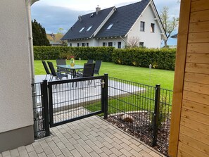 Een terras met een tafel en stoelen, een zwart metalen hek en een verzorgd gazon.
