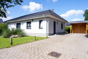 Un bâtiment d’un seul étage, doté d’un toit recouvert de tuiles, d’une allée pavée et d’une porte de garage en bois.