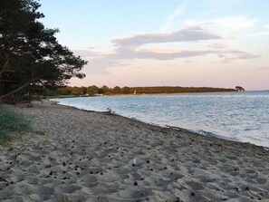 Een strand met een zandstrand, een rustige zee en een verre kustlijn met bomen en een klein eiland.