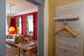 Una habitación con una mesa de comedor, sillas, un sofá, una araña y un perchero de madera en la pared.