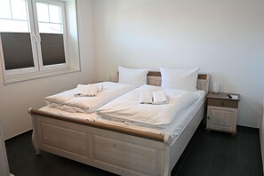Ein Doppelbett mit weißen Laken und Handtüchern, ein Nachttisch mit Lampe und ein kleines Schränkchen.