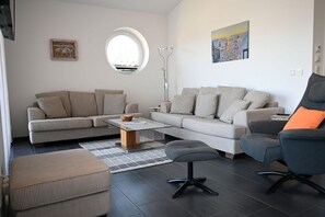 Ein modernes Wohnzimmer mit einer Eckcouch, einem Rundfenster, einer Stehlampe und einem Gemälde an der Wand.