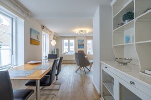 A modern kitchen with white cabinetry, a dining area with a wooden table and chairs, and a view of the city through large windows.