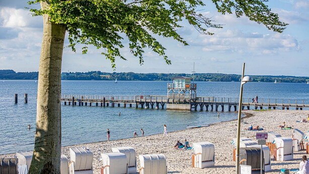 Una spiaggia con lettini, una torretta di salvataggio e un molo che si protende nell'acqua.