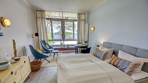 Camera d'albergo moderna con un grande letto, una scrivania e una sedia. Ampie finestre offrono una vista sull'esterno.
