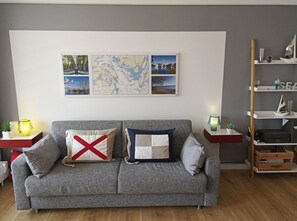 Un sofá gris con dos cojines, un mapa y una estantería con adornos.