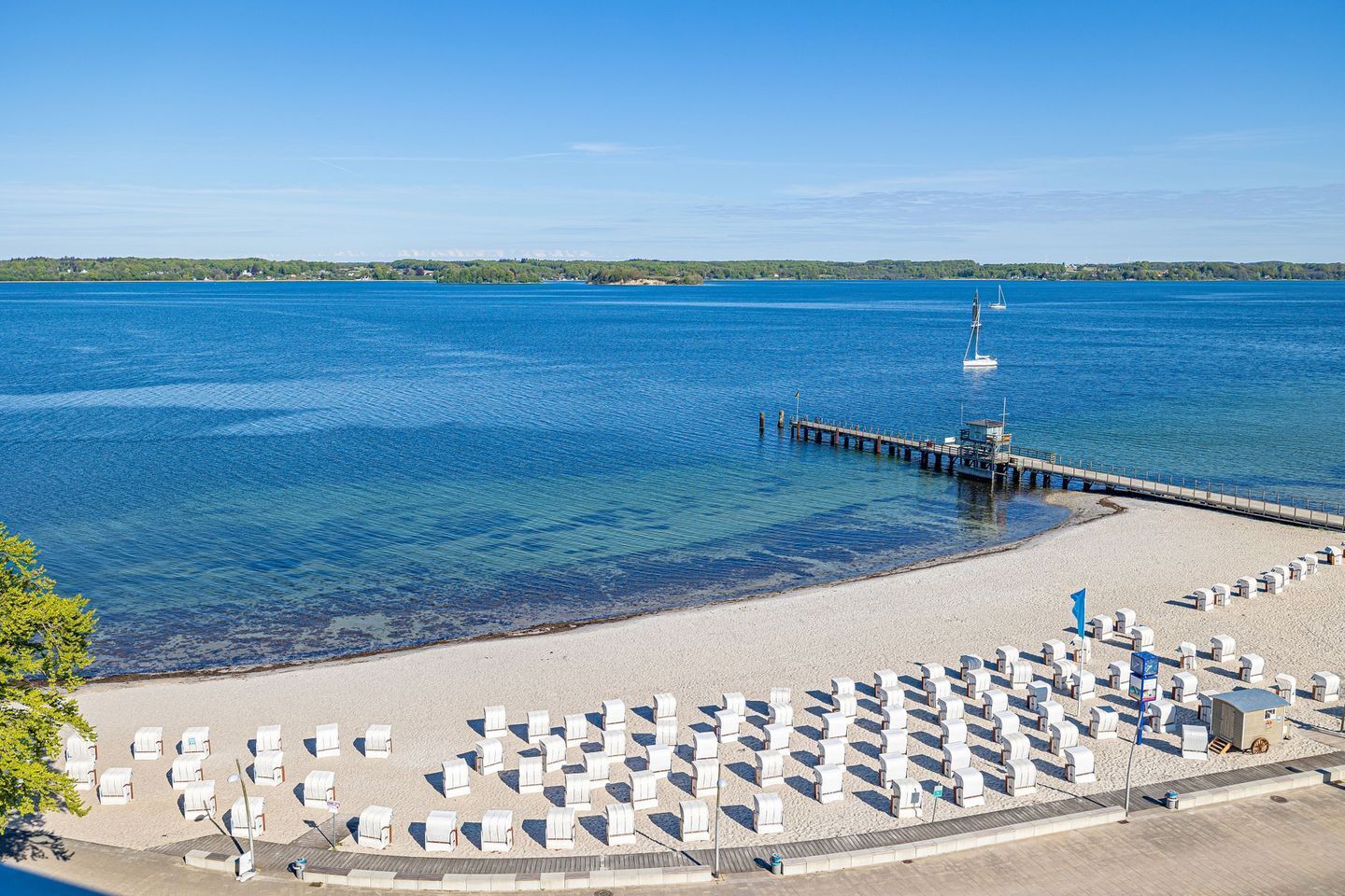 Ein Strand mit Reihen weißer Liegestühle und einem Steg, der ins Wasser führt.