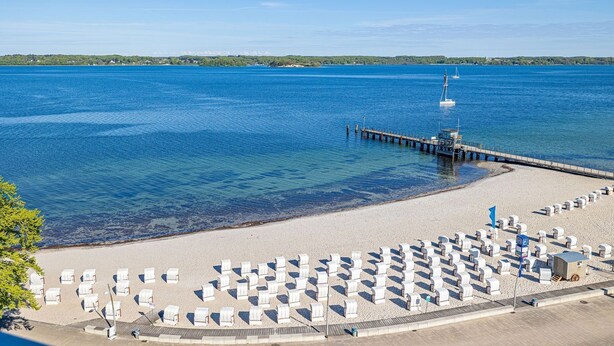 A beach with rows of white lounge chairs and a pier extending into the water. - fewo1846 - Lina K. (App. 504) elegant StudioApartment- sea view up to 4 Per. (Glücksburg (Ostsee))