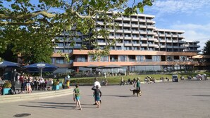 A spacious outdoor area with a modern building in the background, featuring multiple balconies and large windows. - fewo1846 - Lina K. (App. 504) elegant StudioApartment- sea view up to 4 Per. (Glücksburg (Ostsee))