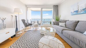A modern living room with a sofa, chairs, a coffee table, and a view of the sea. - fewo1846 - Lina K. (App. 504) elegant StudioApartment- sea view up to 4 Per. (Glücksburg (Ostsee))
