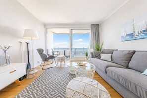 Een moderne woonkamer met een bank, stoelen, een salontafel en uitzicht op zee.