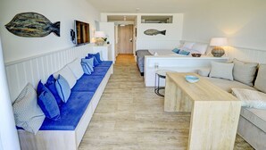 A modern living room with a long blue sofa, a wooden coffee table, and a grey sofa. - fewo1846 - At the Beach - elegant studio apartment with balcony and sea view - (Glücksburg (Ostsee))
