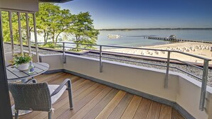 A balcony with a view of a calm lake, a pier, and a boat. - fewo1846 - At the Beach - elegant studio apartment with balcony and sea view - (Glücksburg (Ostsee))