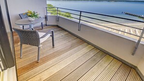 A balcony with a wicker chair and a small table, a view of a calm lake, and a sandy beach. - fewo1846 - Rooftop (App. 604) elegant studio apartment with balcony and sea view (Glücksburg (Ostsee))