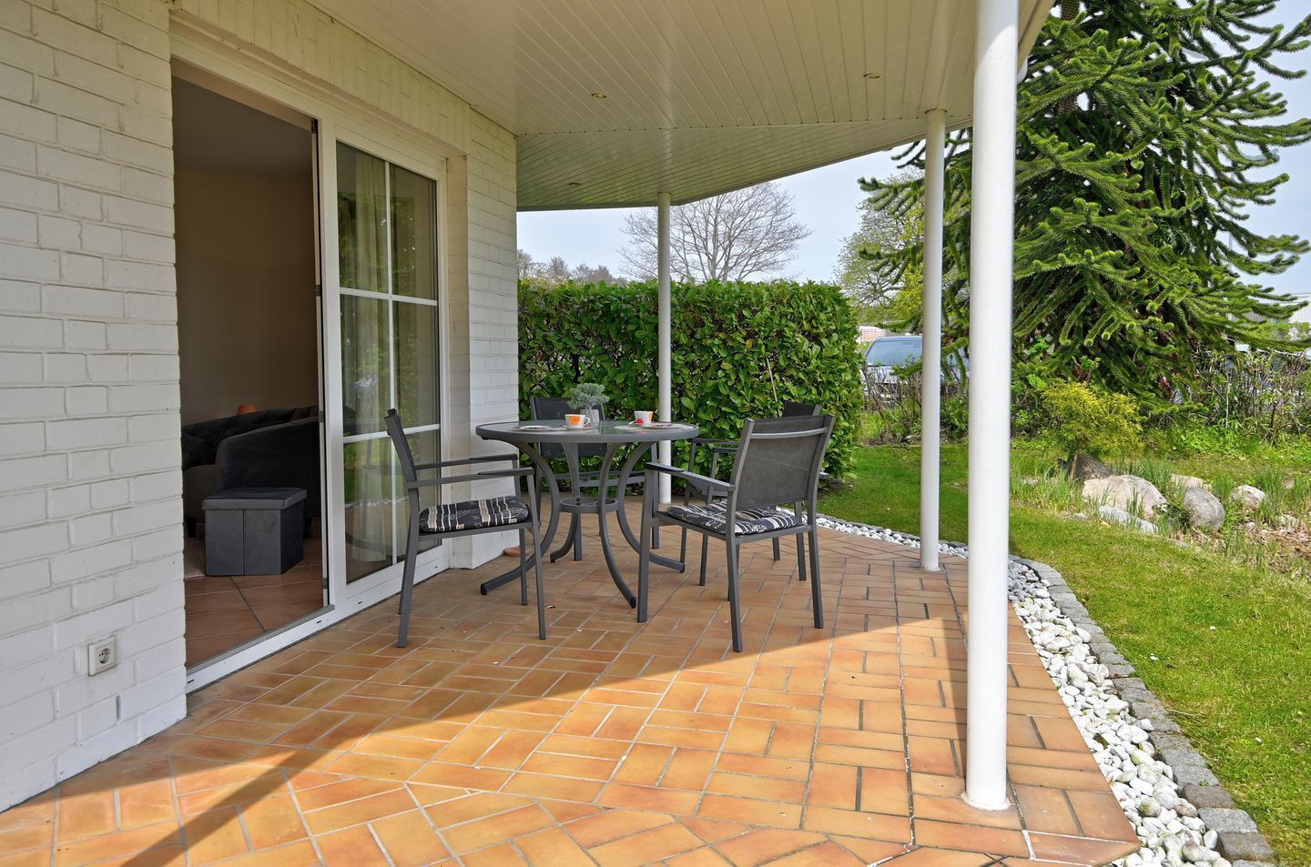 A patio with a table and chairs, a covered area, and a view of the surrounding garden.