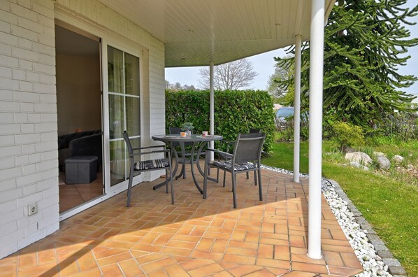 A patio with a table and chairs, a covered area, and a view of the surrounding garden.
