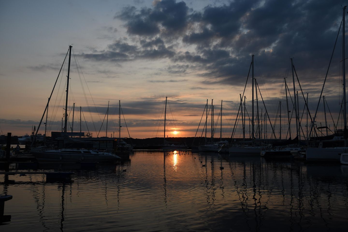Un port de plaisance au coucher du soleil, où sont amarrés de nombreux voiliers.
