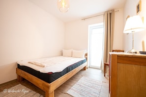 Une chambre à coucher avec un lit en bois, une table de chevet avec une lampe, une fenêtre avec des rideaux et une porte.