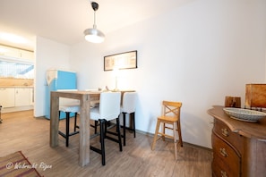 Un coin repas avec une table et des chaises en bois, un petit tabouret, un meuble contenant un bol et un luminaire fixé au mur.
