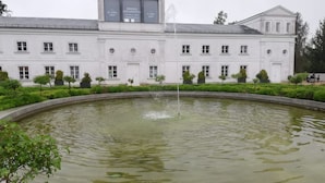 A large white building with a fountain in the center of a circular pond, surrounded by neatly trimmed bushes and trees. - Vacation apartment "Don't forget mine" - Holiday apartment "Don't forget mine" - (Putbus)