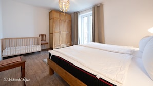 A bedroom with a large bed, a wooden wardrobe, a crib, and a desk. - Vacation apartment "Don't forget mine" - Holiday apartment "Don't forget mine" - (Putbus)