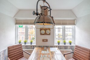 Un coin repas avec une table en bois rustique, des chaises en cuir, un luminaire suspendu de style vintage et une horloge murale.