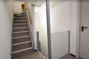 Eine schmale Treppe mit hölzernen Stufen und einem Metallgeländer, die zu einer weißen Tür mit schwarzem Griff führt.