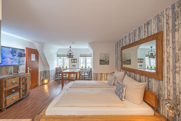 Une chambre à coucher avec un grand lit, une commode en bois, une table à manger avec des chaises et un grand miroir.