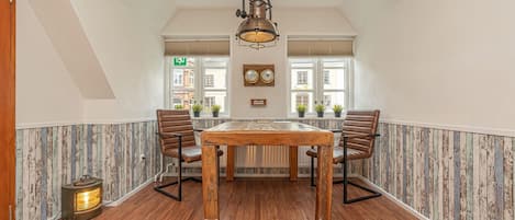 A dining area with a wooden table and chairs, a hanging light fixture, and a view of the street through large windows.