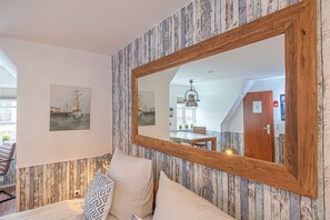 Ein Schlafzimmer mit einem spiegelnden, holzgerahmten Wandbild, einem Bett mit Kissen und Blick auf den Essbereich im Spiegel.