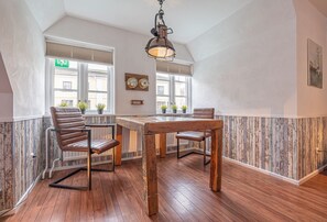 A dining area with a wooden table and chairs, a hanging light fixture, and a view of the street through large windows.