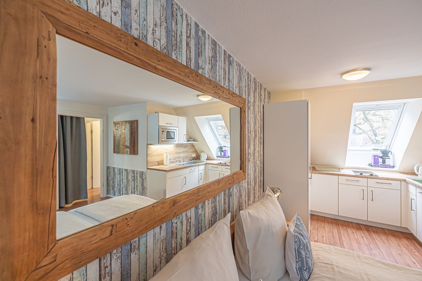 Ein Schlafzimmer mit großem Spiegel, Holz-Kopfteil und Blick auf eine Küche und einen Balkon.