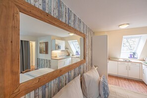 A bedroom with a large mirror, wooden headboard, and a view of a kitchen and balcony.