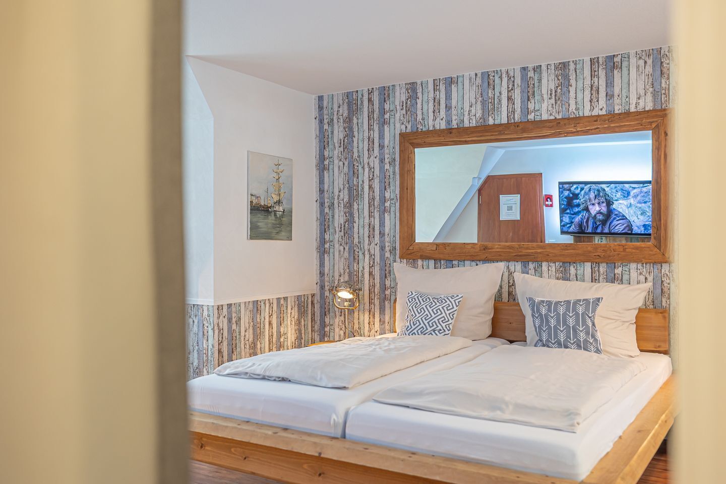 A bedroom with a bed, a wooden headboard, a large mirror, and a wall-mounted TV.