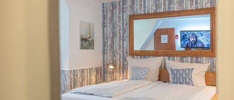 A bedroom with a bed, a wooden headboard, a large mirror, and a wall-mounted TV.
