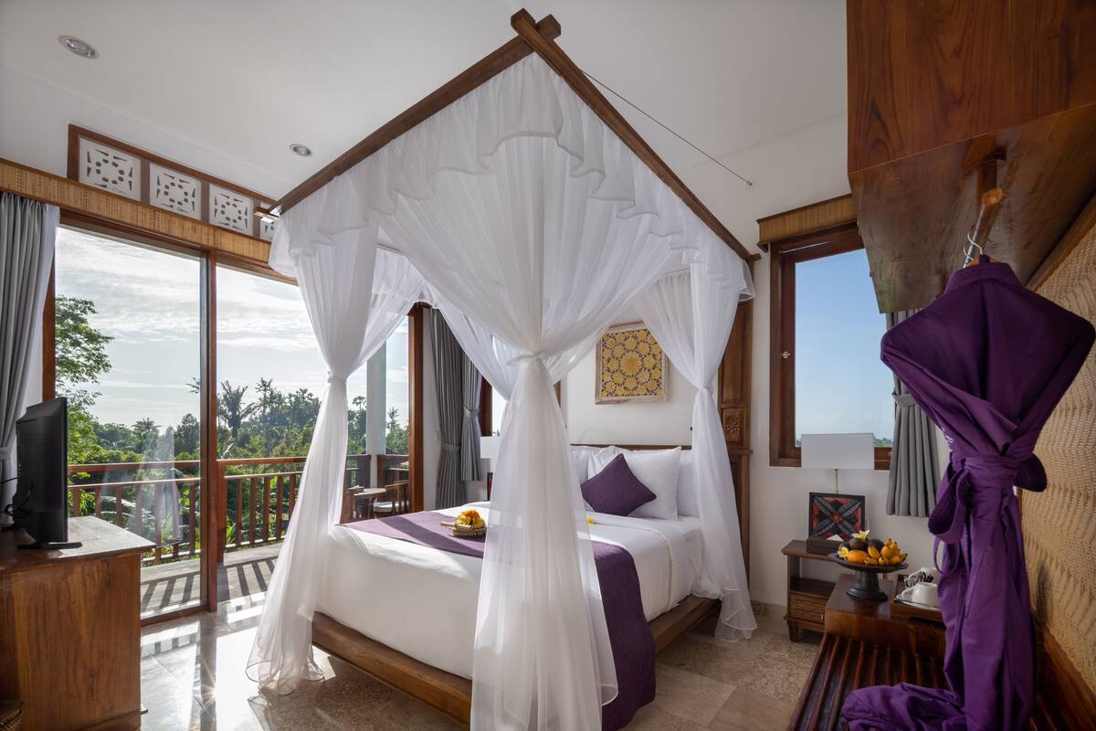 Een slaapkamer met een hemelbed, een balkon met uitzicht en een houten bureau met een televisie.