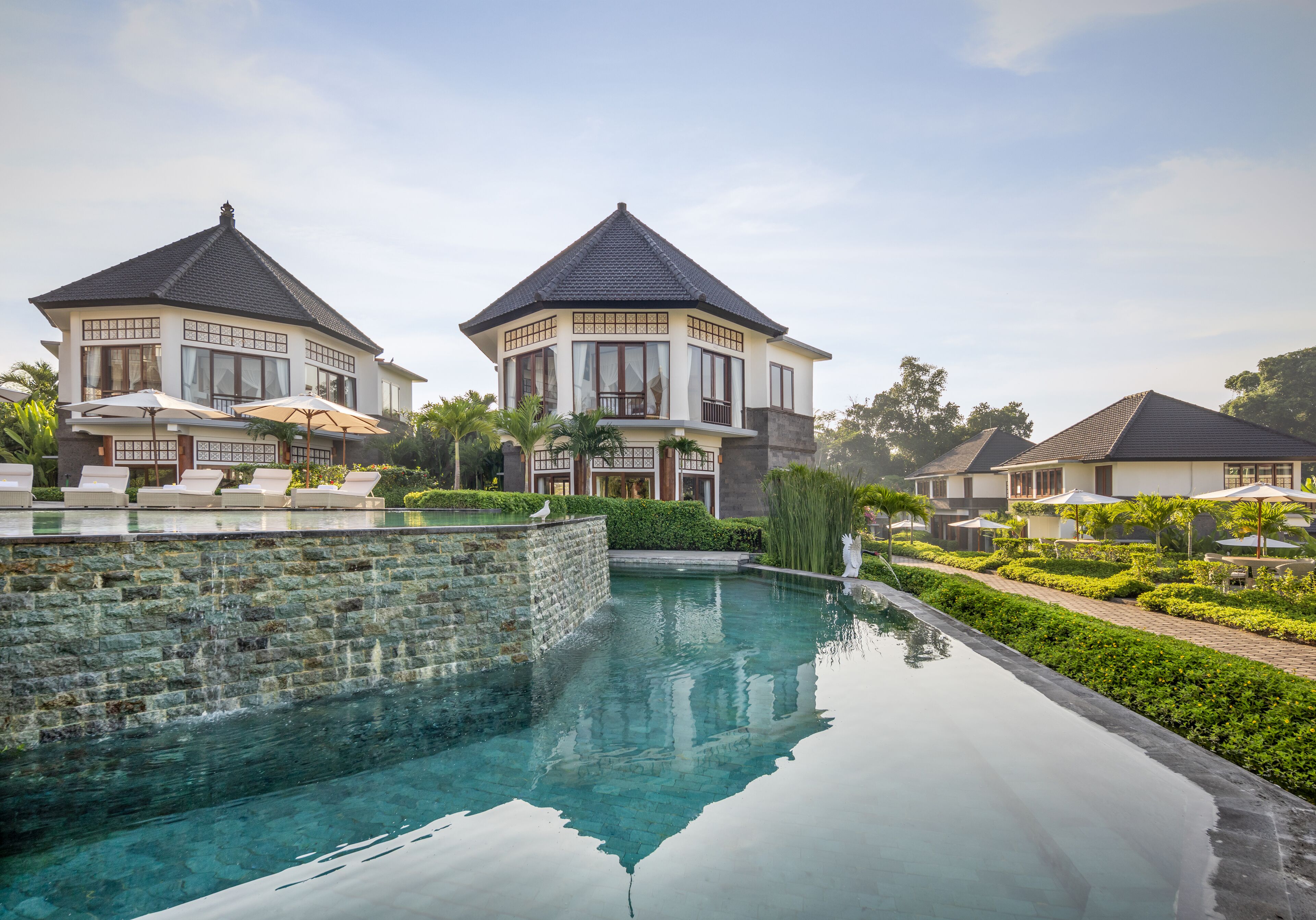 A resort with a swimming pool, lounge chairs, and two main buildings with a traditional architectural style.