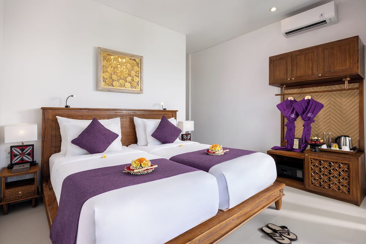 Een hotelkamer met twee bedden, een houten hoofdbord, een kleine tafel met een lamp, een decoratieve wandversiering en een kledingkast.