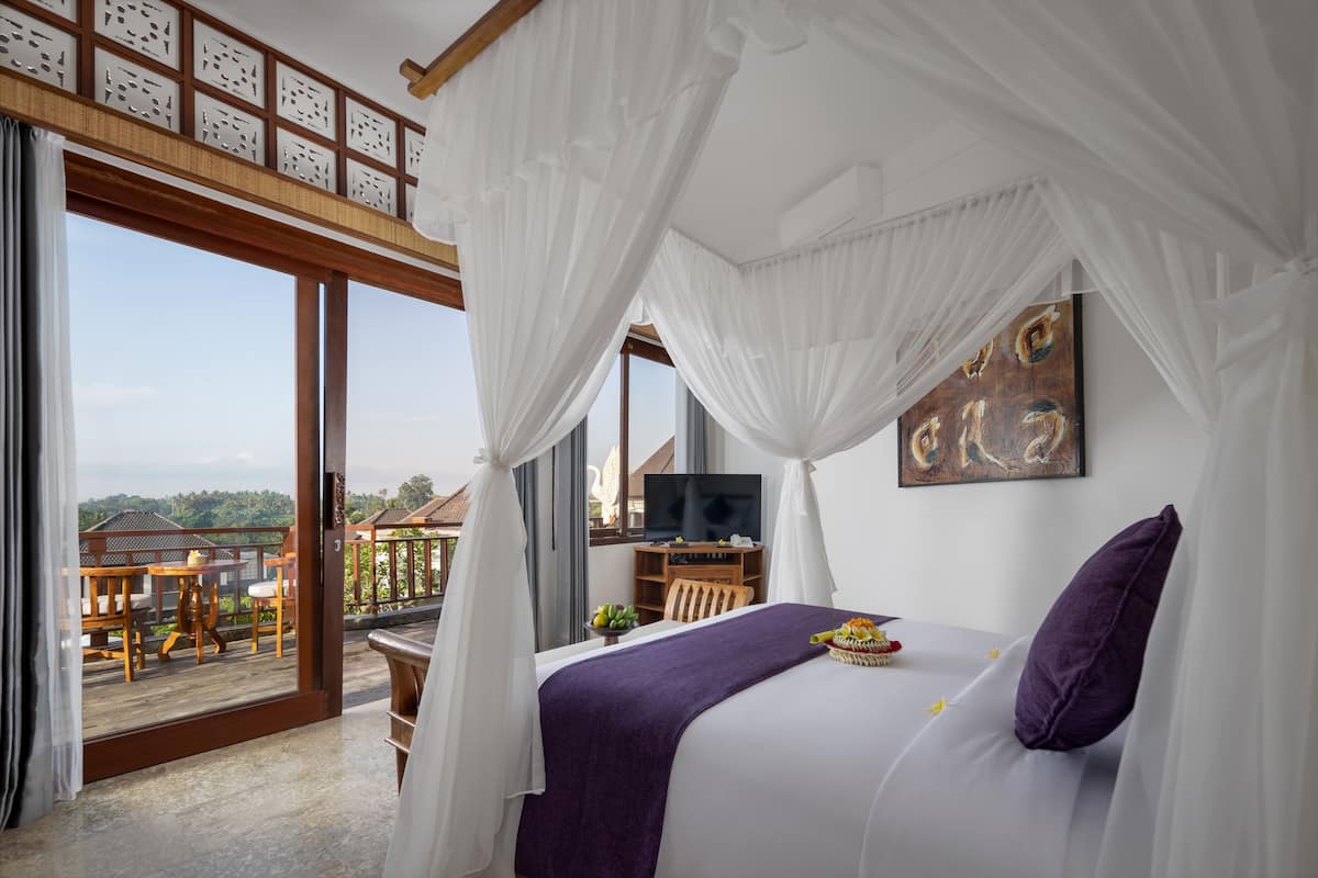 Een slaapkamer met een groot bed, een televisie en een balkon met een tafel en stoelen.