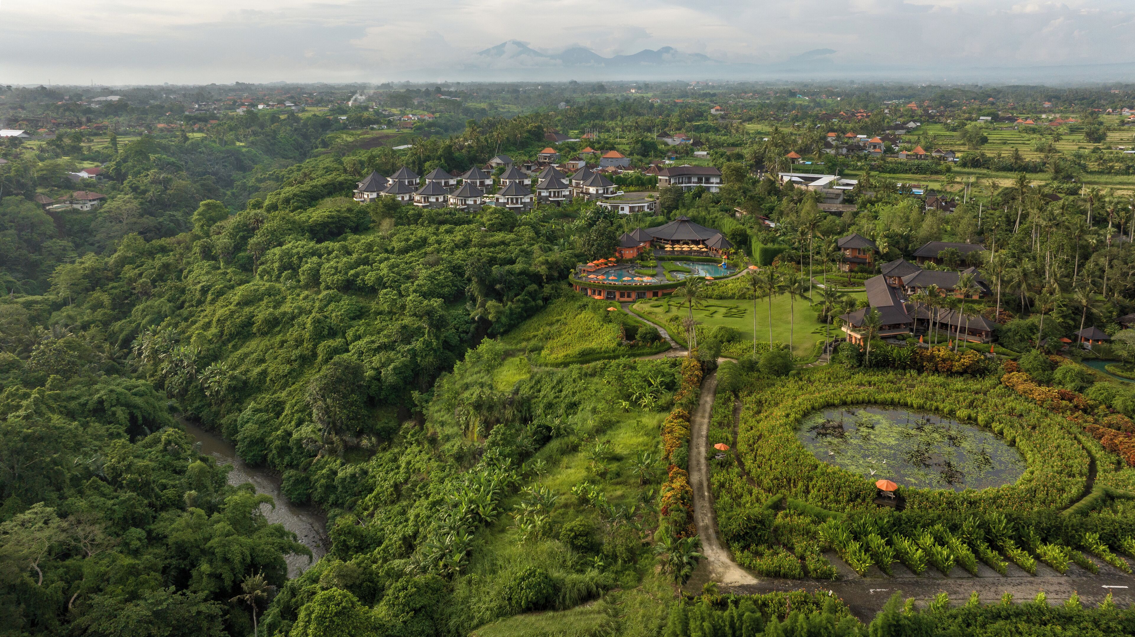 An aerial view of a resort with multiple buildings, lush greenery, and a swimming pool.