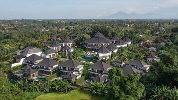 A residential area with multiple houses featuring dark roofs and white walls, surrounded by lush greenery and palm trees.