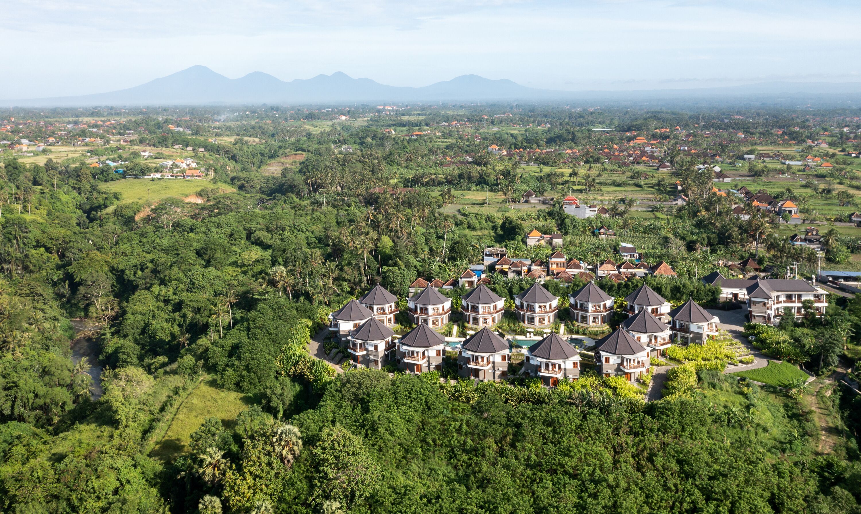Un quartier résidentiel composé de plusieurs maisons, entouré d’une végétation luxuriante et dominé par un paysage montagneux.
