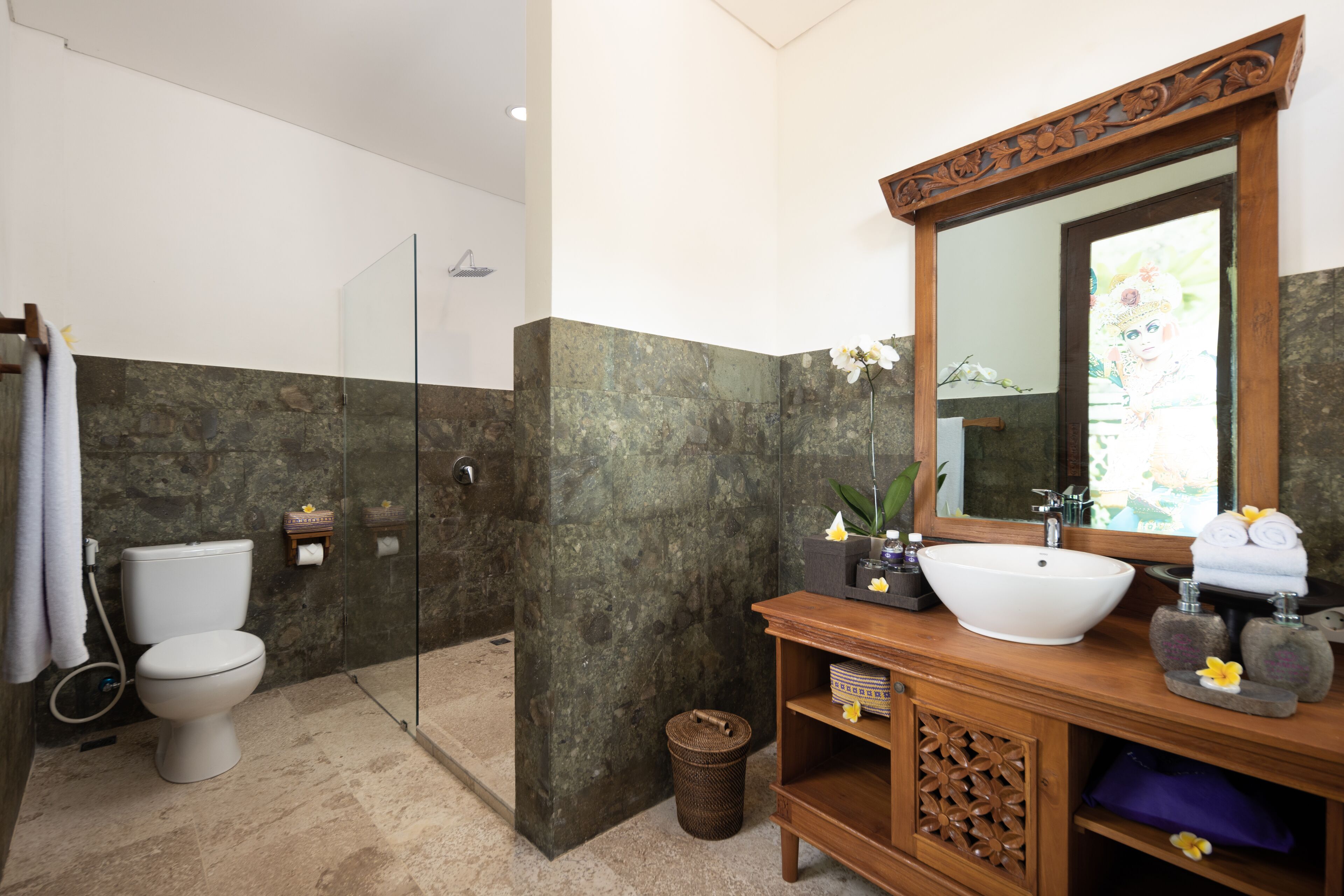 Een badkamer met een glazen douchecabine, een wit toilet, een houten wastafelmeubel met een grote spiegel en een witte wasbak.