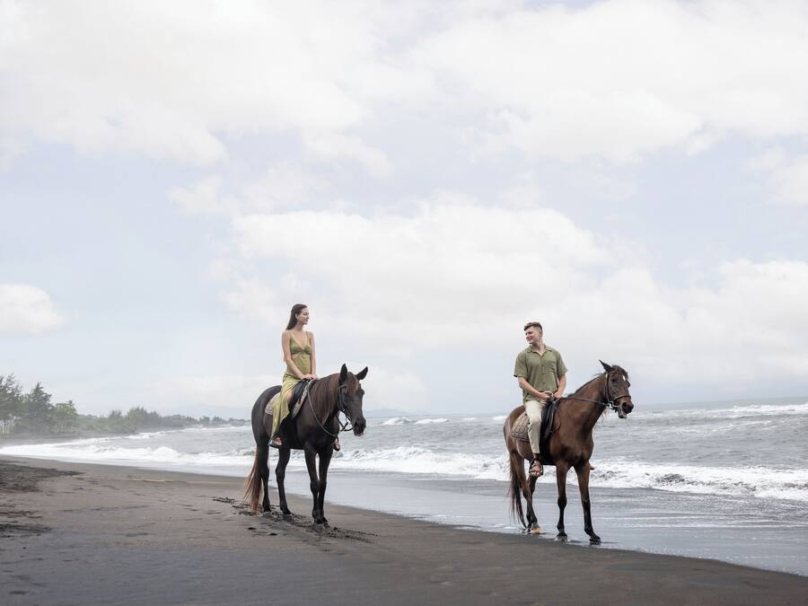 Two people riding horses on a beach with the ocean in the background.
