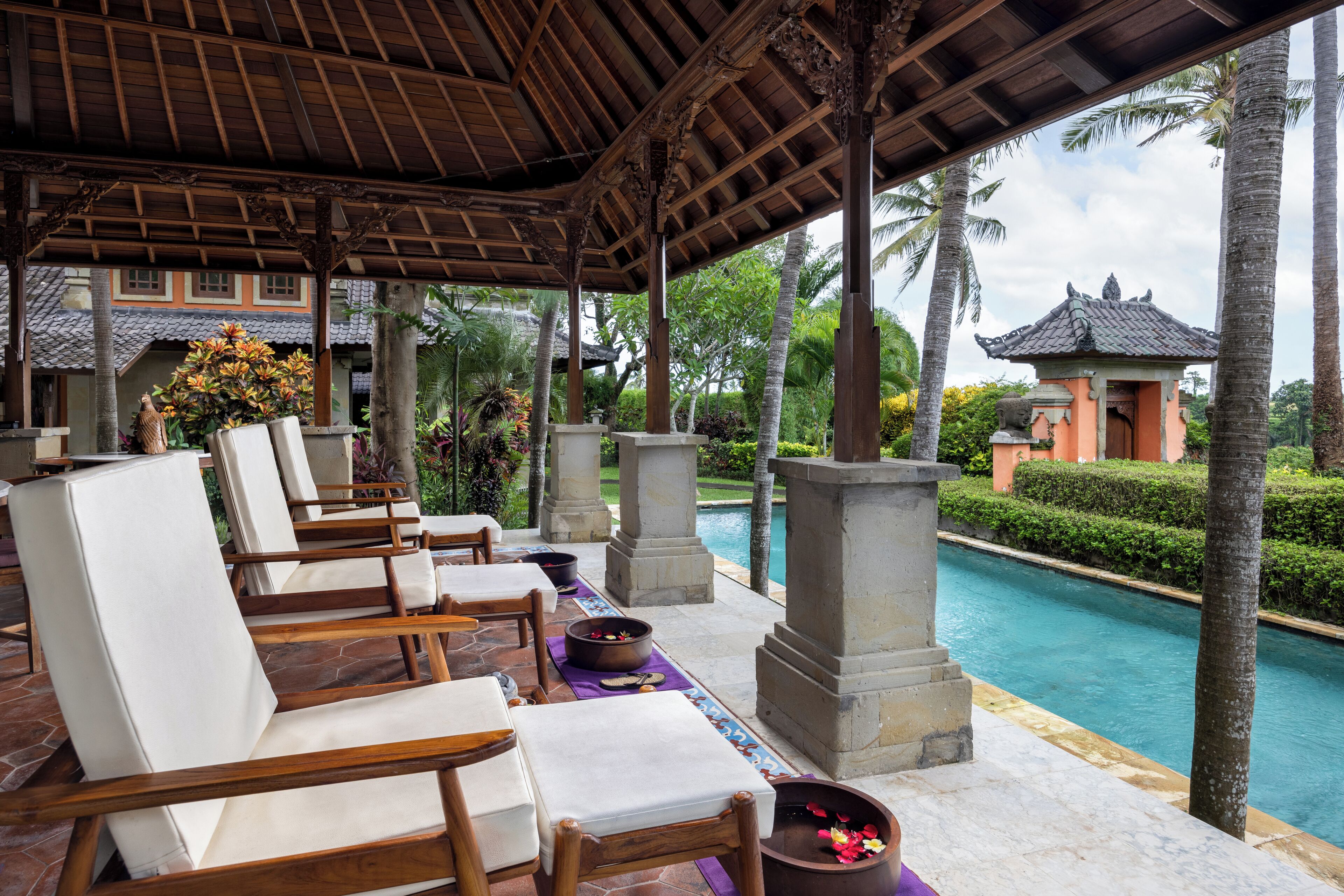 A covered lounge area with wooden chairs and a pool view.