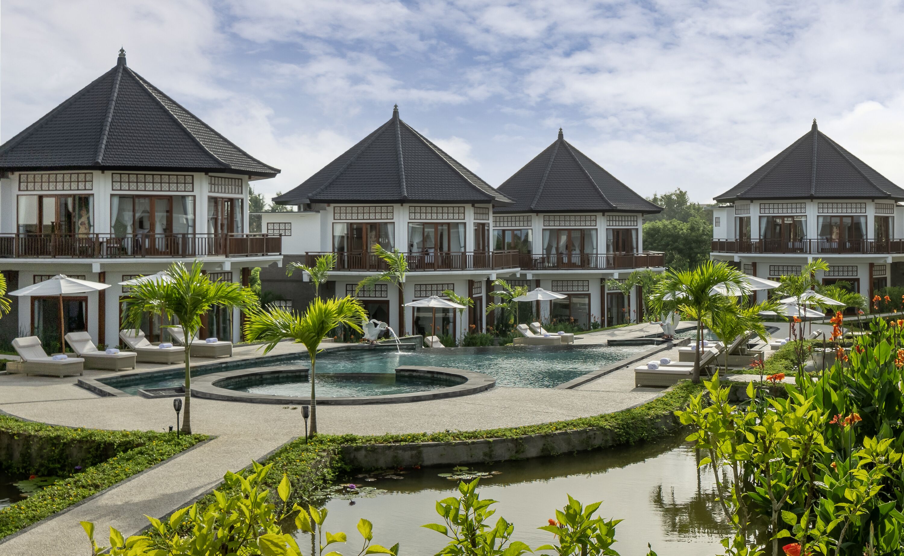 Un resort con varias construcciones, una piscina central y follaje circundante.