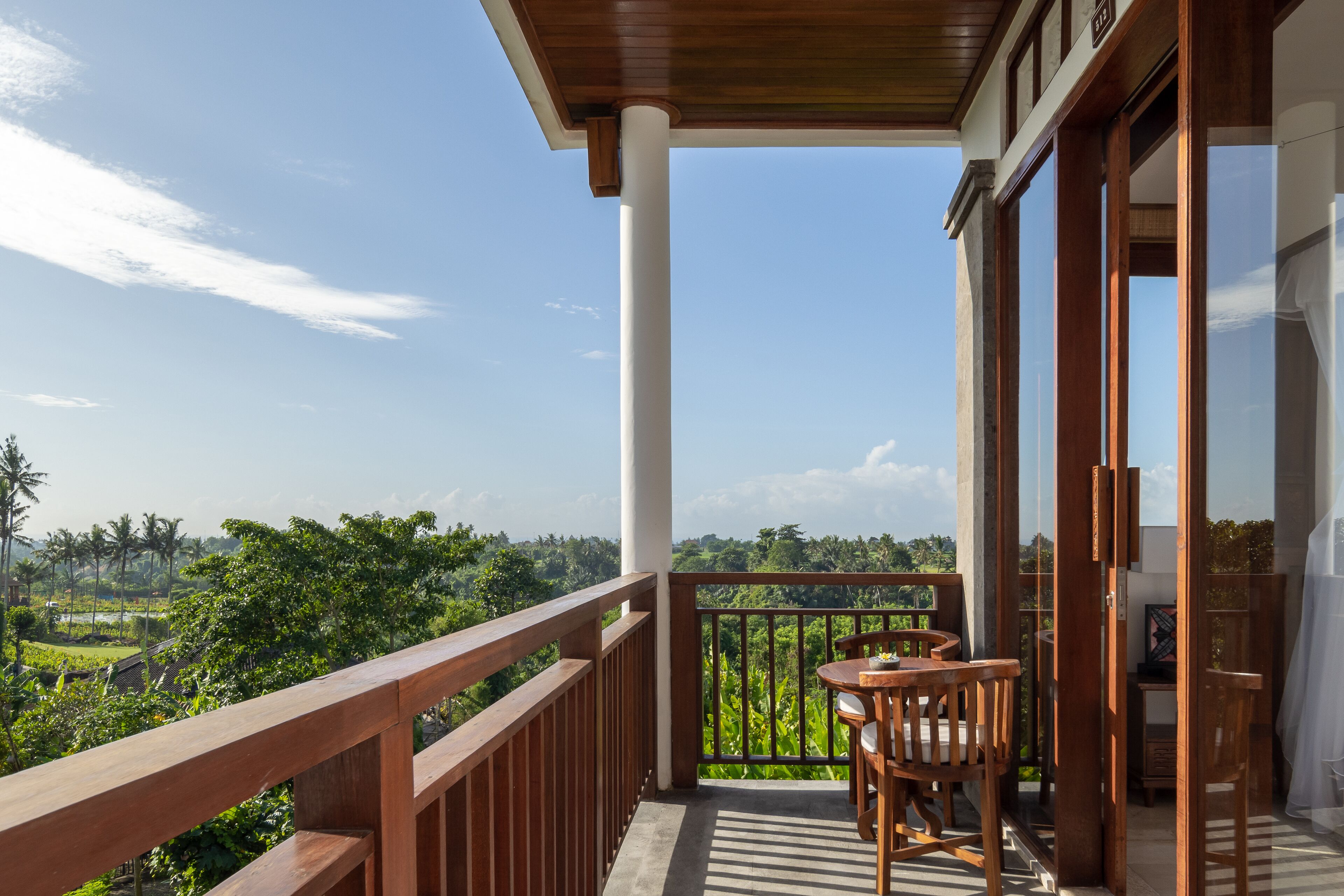 Un balcón con baranda de madera, una mesa con sillas y vistas a un paisaje exuberante.