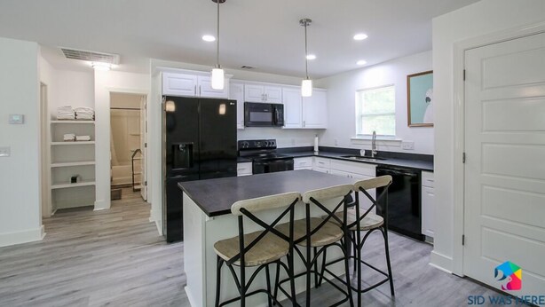A modern kitchen with white cabinets, a black refrigerator, a microwave, and a stove. There are three bar stools at the island.
